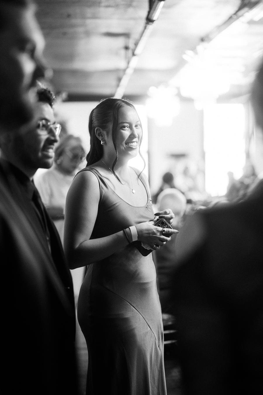 Black and white photo of a woman smiling at an event, surrounded by people in an indoor setting.