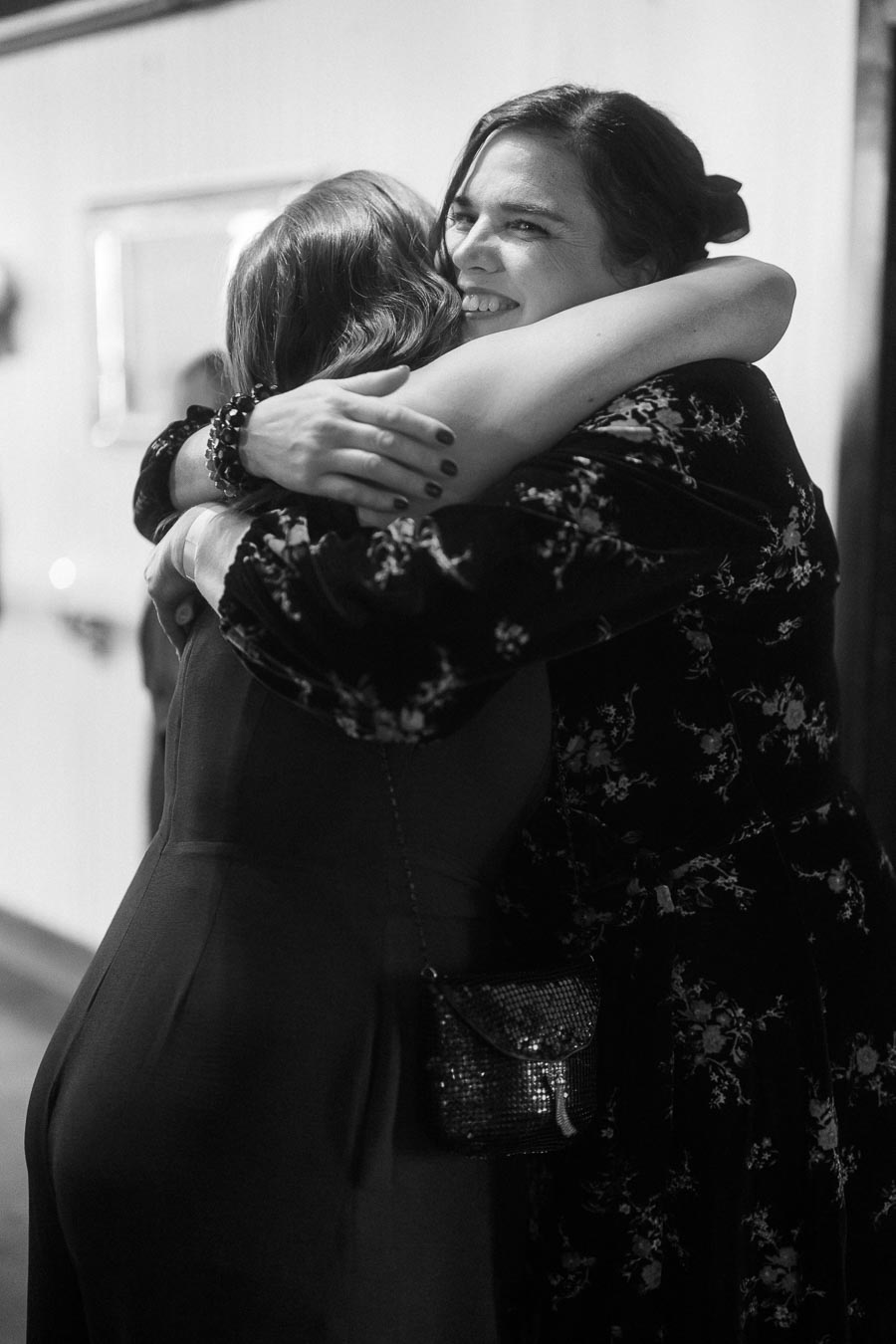 Two women embracing warmly at an event, showcasing friendship and joy, captured in black and white photography.