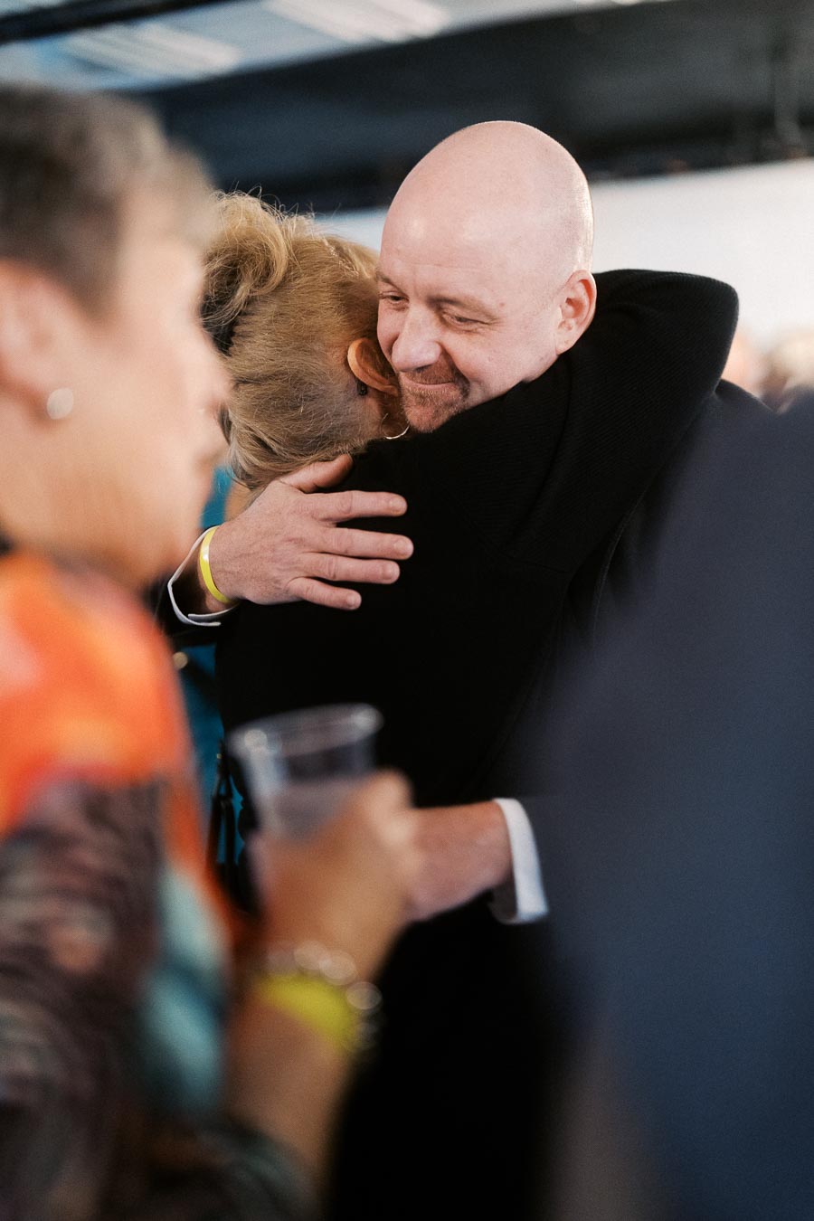 A heartfelt embrace between two people at a social gathering, with blurred guests in the background, conveying warmth and connection.