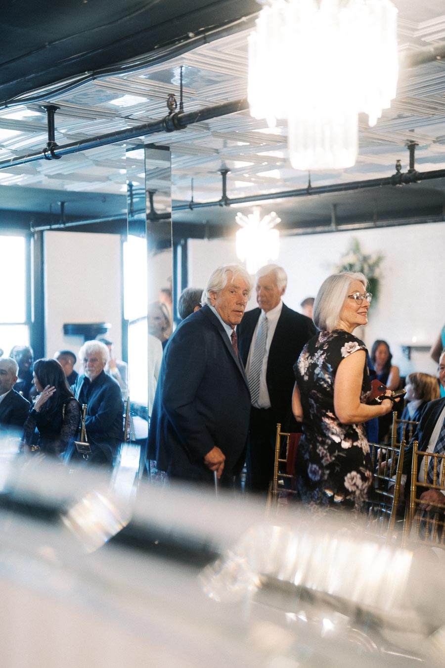 Group of elegantly dressed people conversing in a sophisticated event setting, featuring modern decor and ambient lighting.