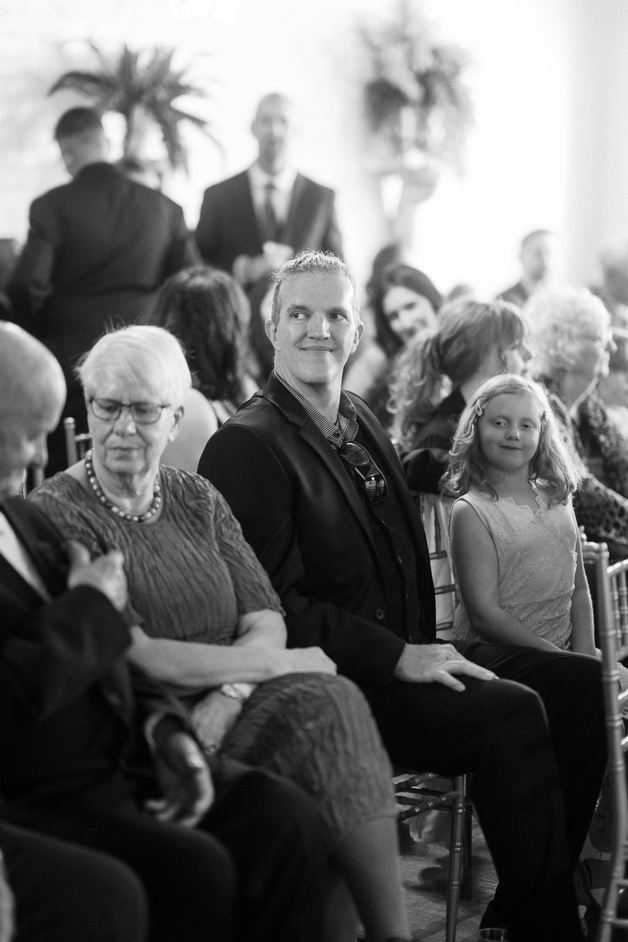 Black and white image of a well-dressed group of people seated in a formal setting, smiling and engaged.