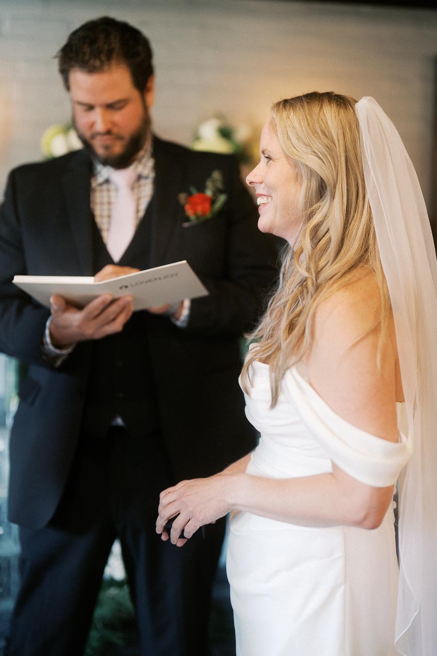 Bride smiling during wedding ceremony as officiant reads vows.