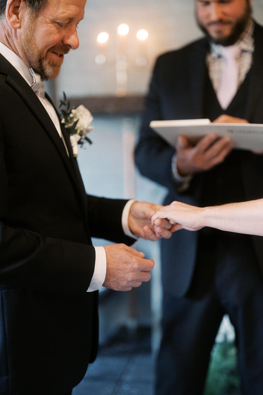 Groom exchanging rings during intimate wedding ceremony with officiant in background.