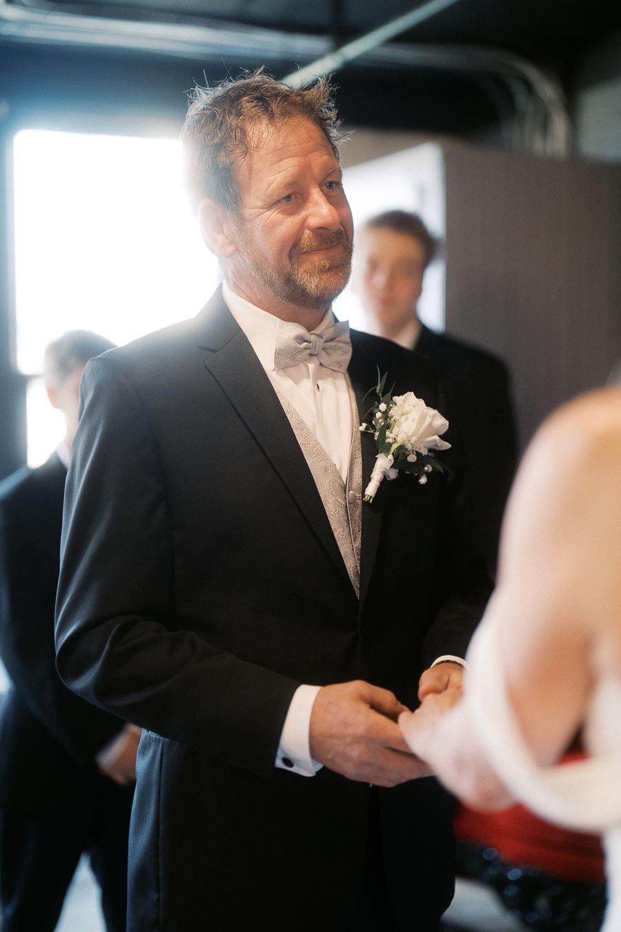 A groom in a black tuxedo, wearing a white boutonniere, shares an emotional moment during a wedding ceremony.