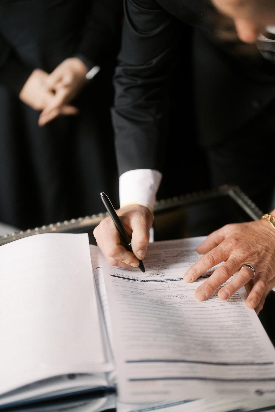 Person in a suit signing a document on a table, emphasizing business and legal agreement themes.