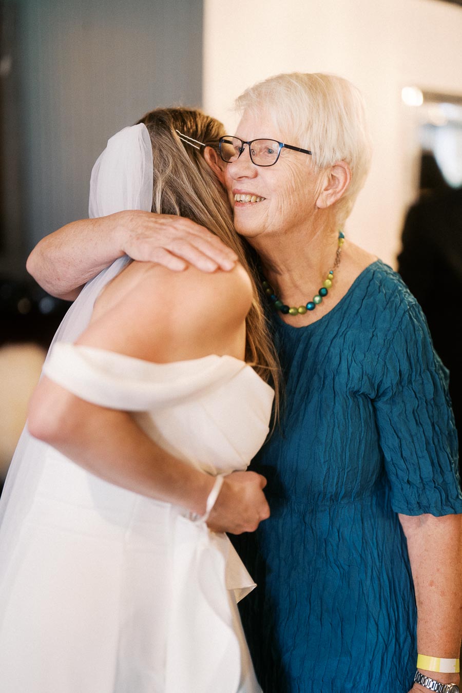 Elderly woman in blue dress embracing a bride in wedding attire, capturing a heartfelt moment of joy and connection during a wedding celebration.