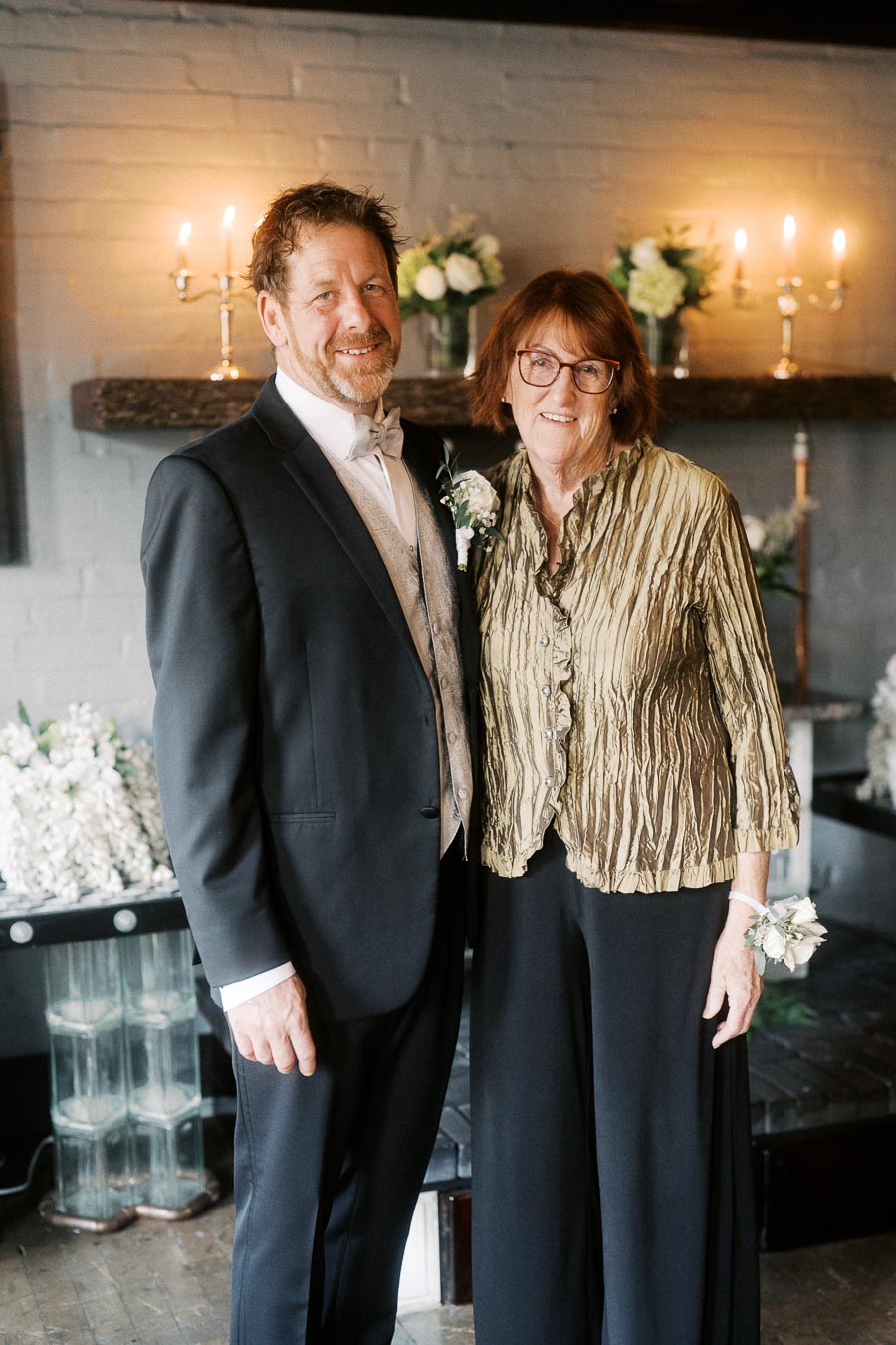 Elegant couple posing at a formal event, with decorative flowers and candlelight, conveying a warm and celebratory atmosphere.