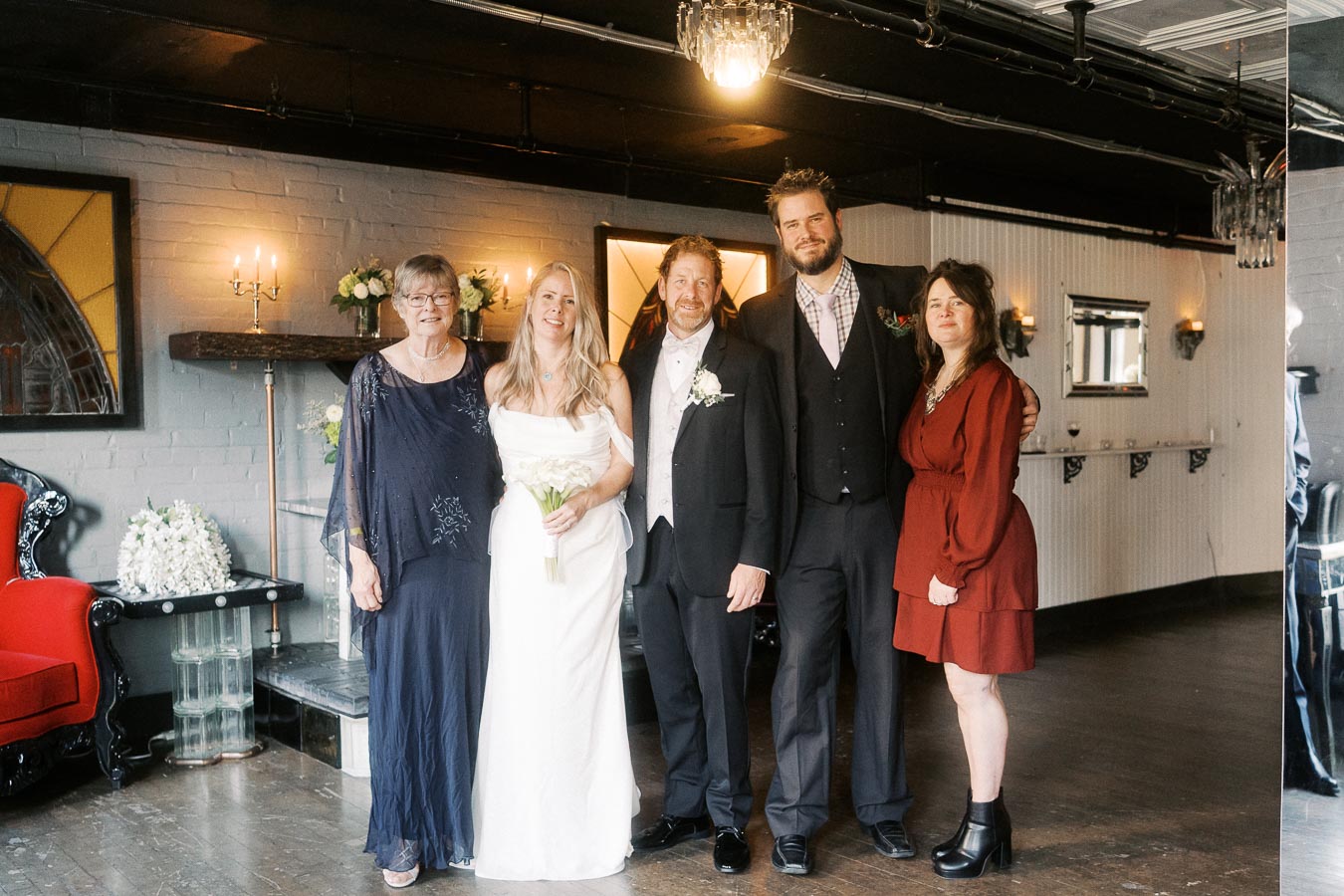 A group of people dressed in formal attire standing together in a warmly lit room with elegant decor, including multiple candles and floral arrangements.