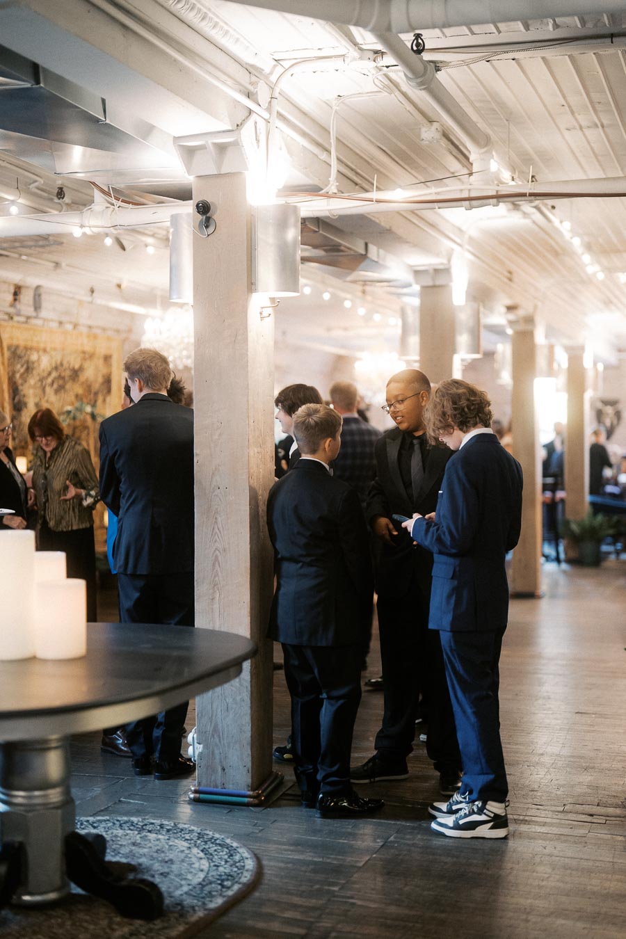 Group of people in formal attire having a conversation at an elegant indoor event space with ambient lighting and wooden decor.