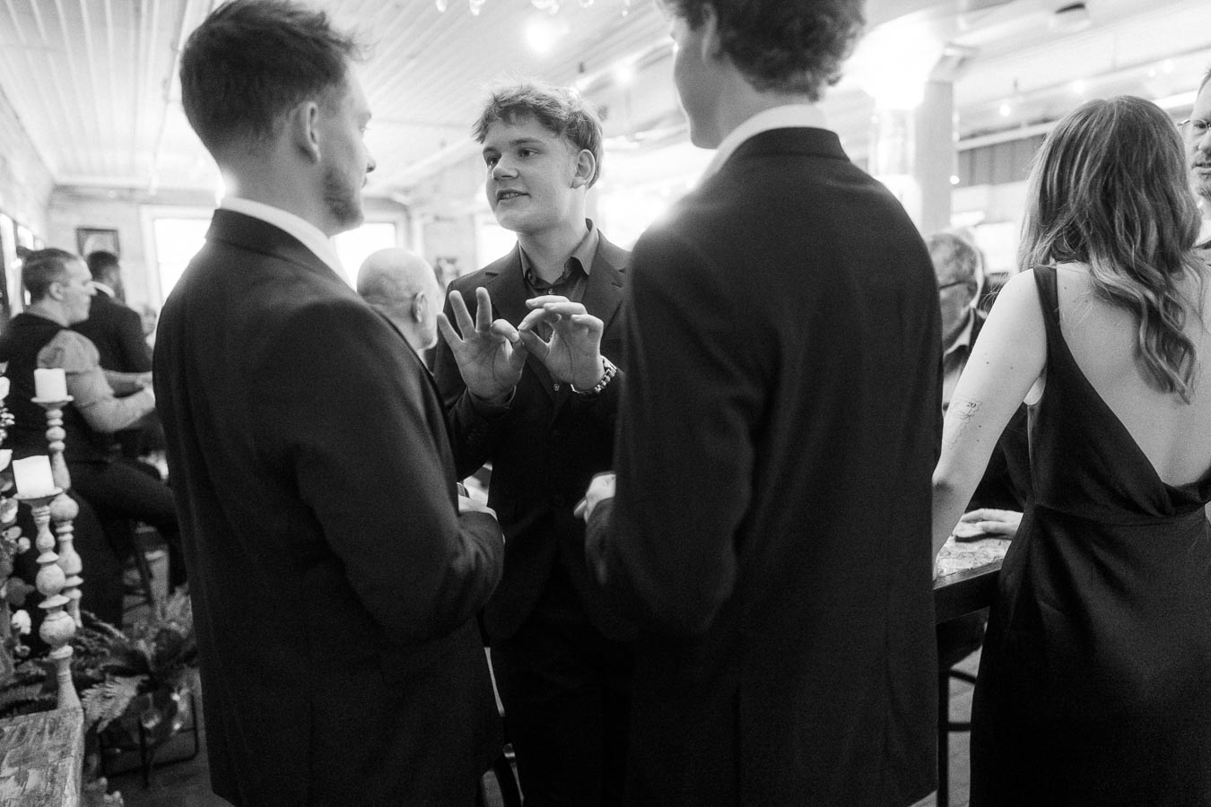 Group of people in formal attire engaged in conversation at an indoor social event.