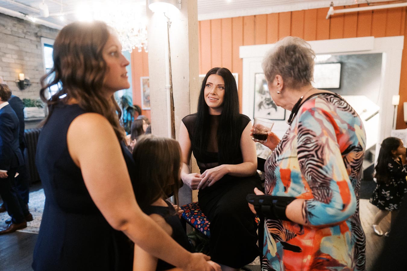 A group of women socializing at an indoor gathering, featuring casual conversations and colorful attire, with a warm and inviting atmosphere in a well-decorated room.