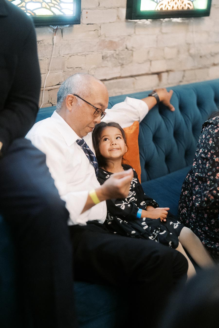 A grandfather and granddaughter share a tender moment on a cozy blue couch, the girl looking up adoringly at the man, showcasing a familial bond in a warmly lit room.