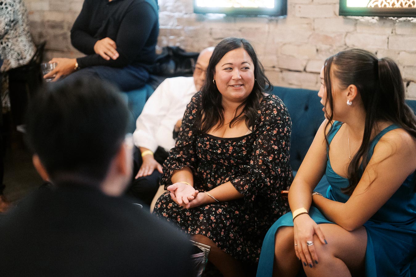 Group of people having a lively conversation at a social gathering, seated in a cozy indoor setting with exposed brick walls and comfortable seating.