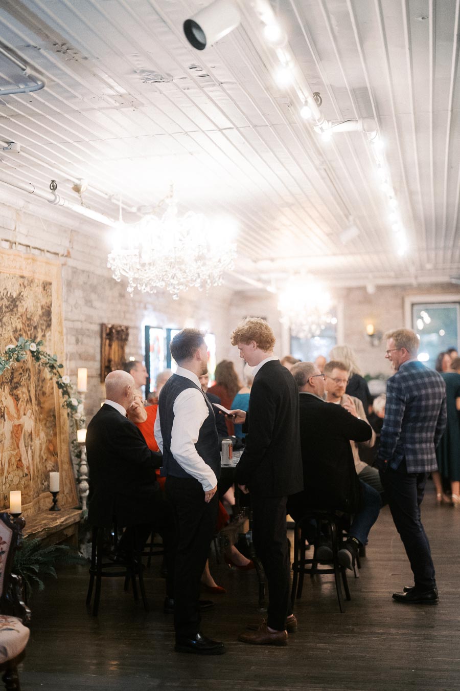 Formal gathering in an elegantly decorated room with chandeliers; people are engaged in conversation, creating a lively and sophisticated atmosphere.