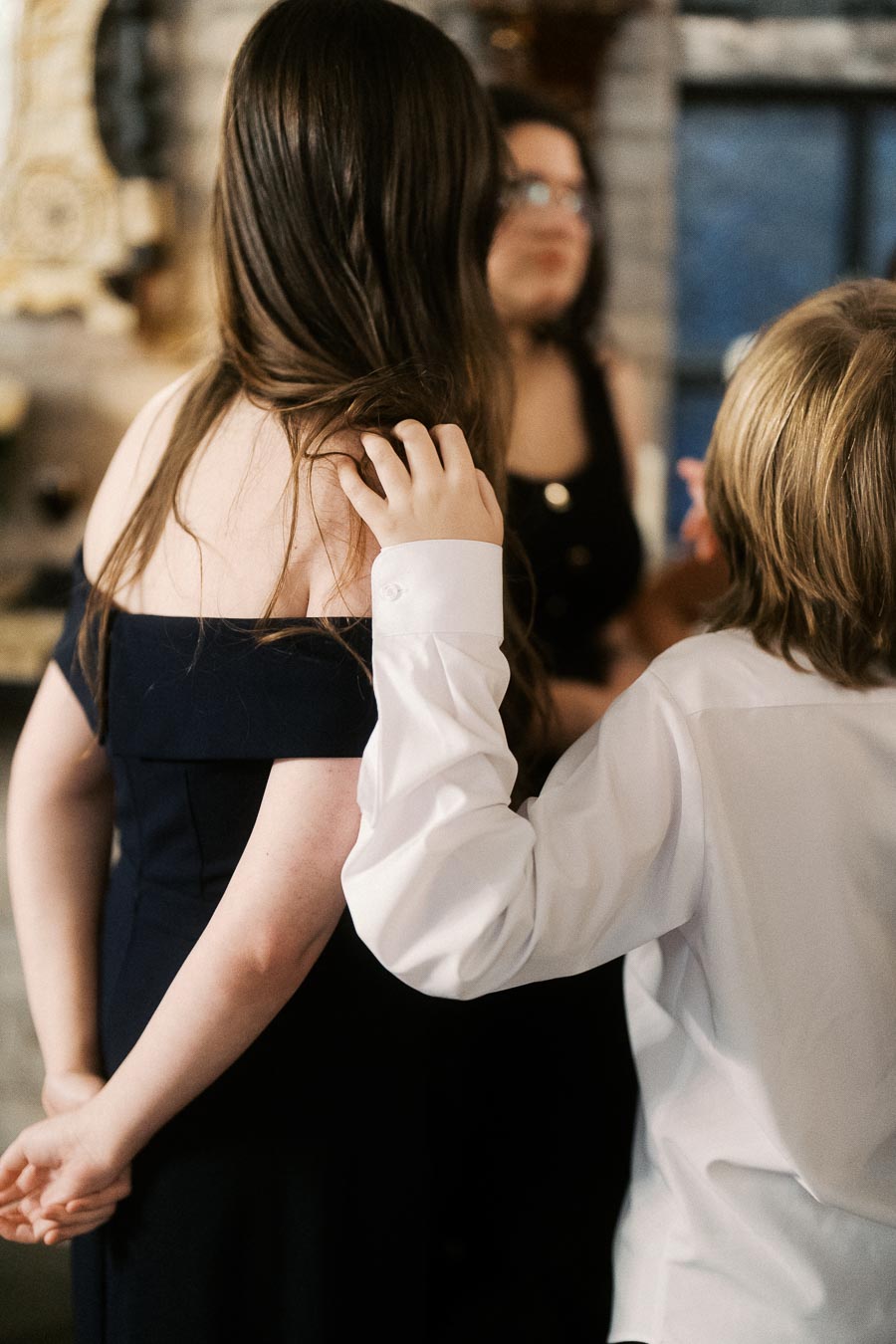 Young people dressed in formal attire at a social event, with one placing a hand on another's shoulder, creating a relaxed and friendly atmosphere.