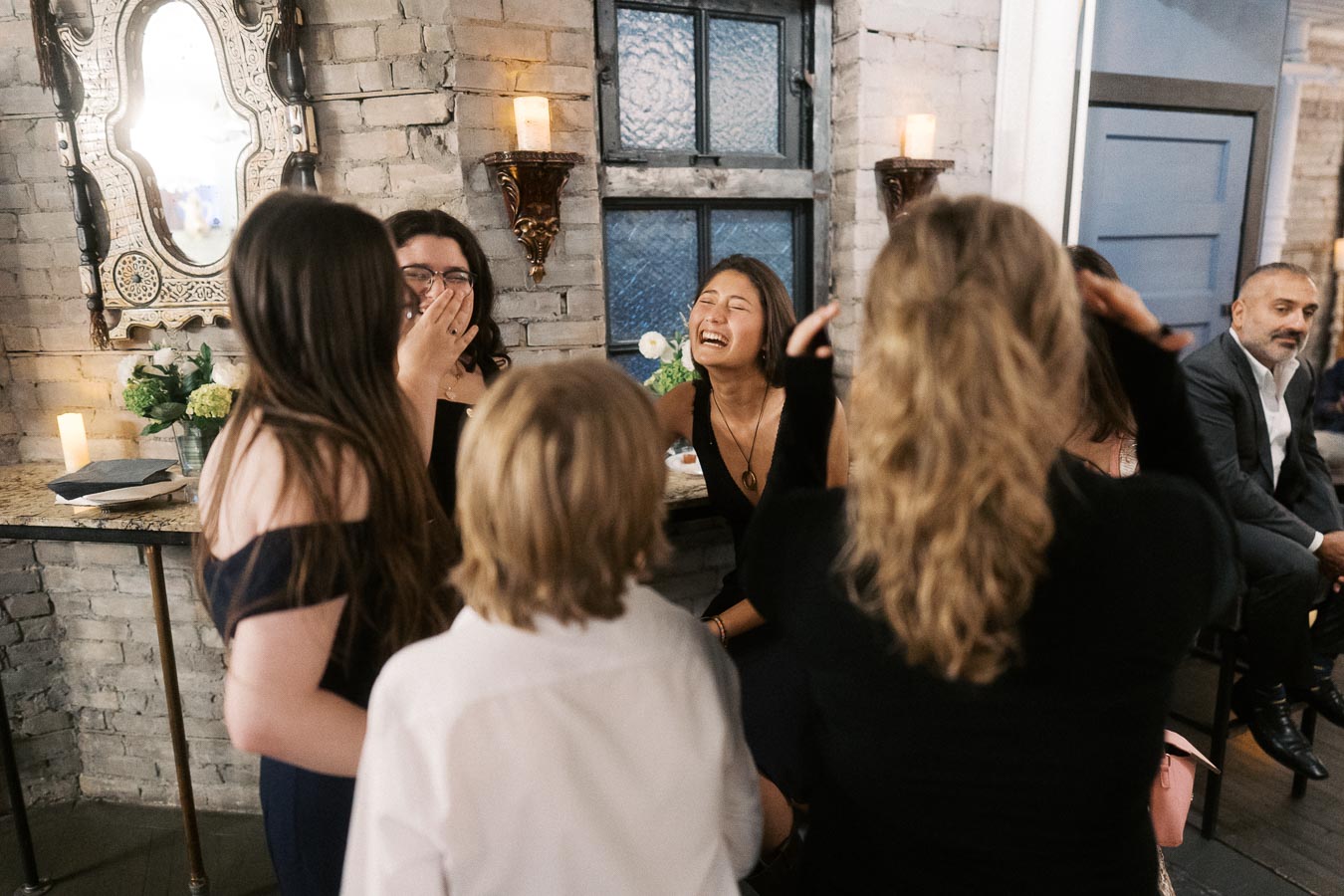 Group of friends sharing laughter at a social gathering in a warmly lit room with decorative walls and candles.