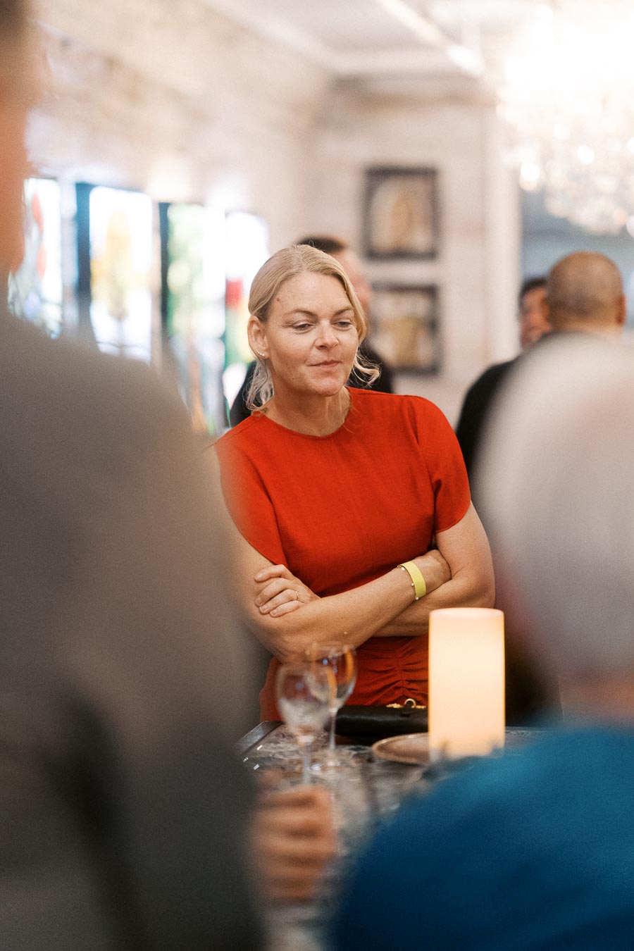 Woman in a red dress attending a social gathering at a modern venue, with ambient lighting and other people in the background.