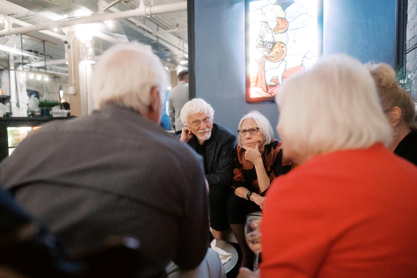 Group of older adults engaged in conversation at a social gathering, seated in a cozy, well-lit indoor environment.