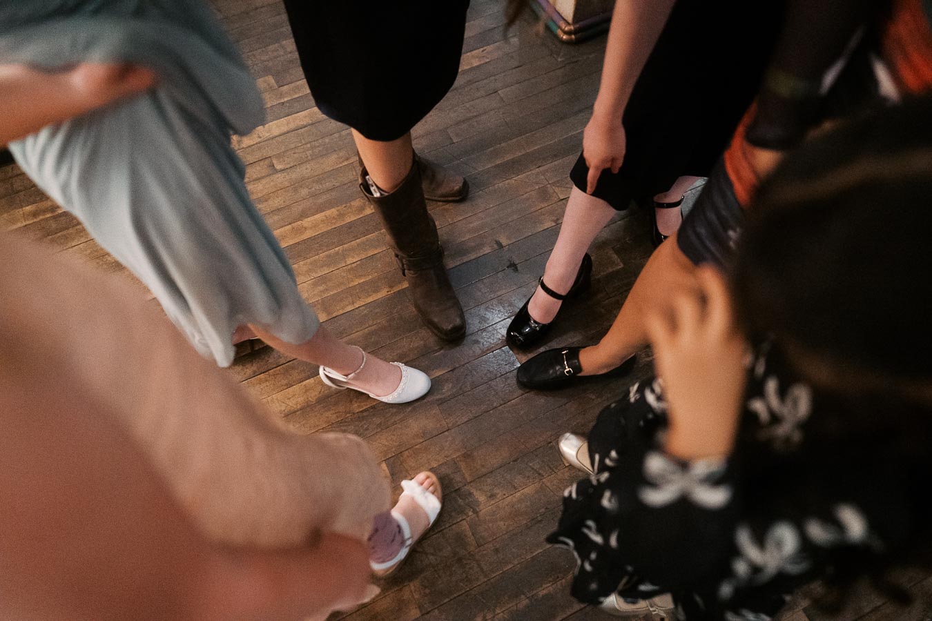 A group of people standing in a circle wearing different styles of shoes on a wooden floor, highlighting diverse footwear choices and social gathering vibes.