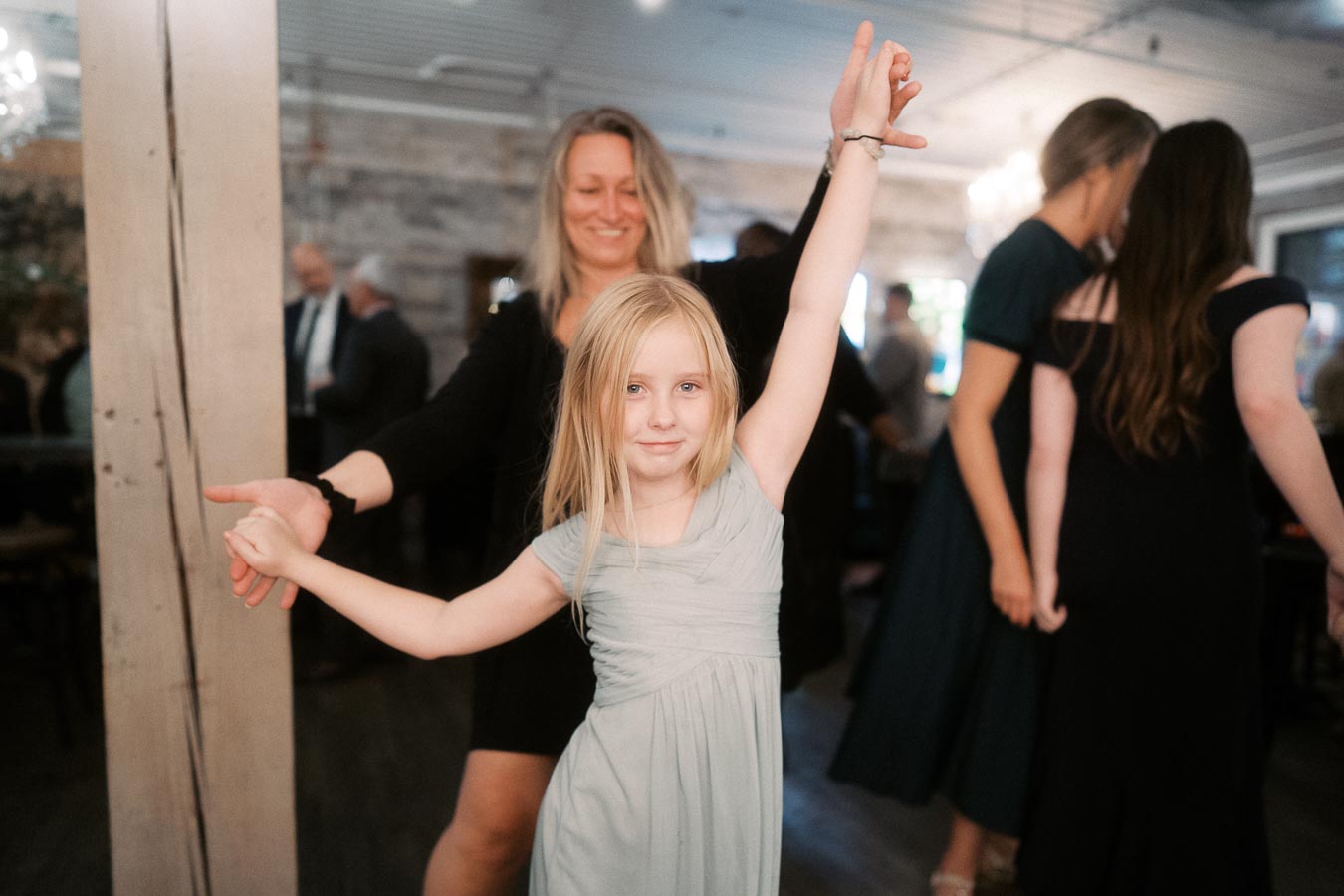 A joyful young girl in a light dress dancing with an adult at a lively event, capturing the happiness and energy of the occasion.