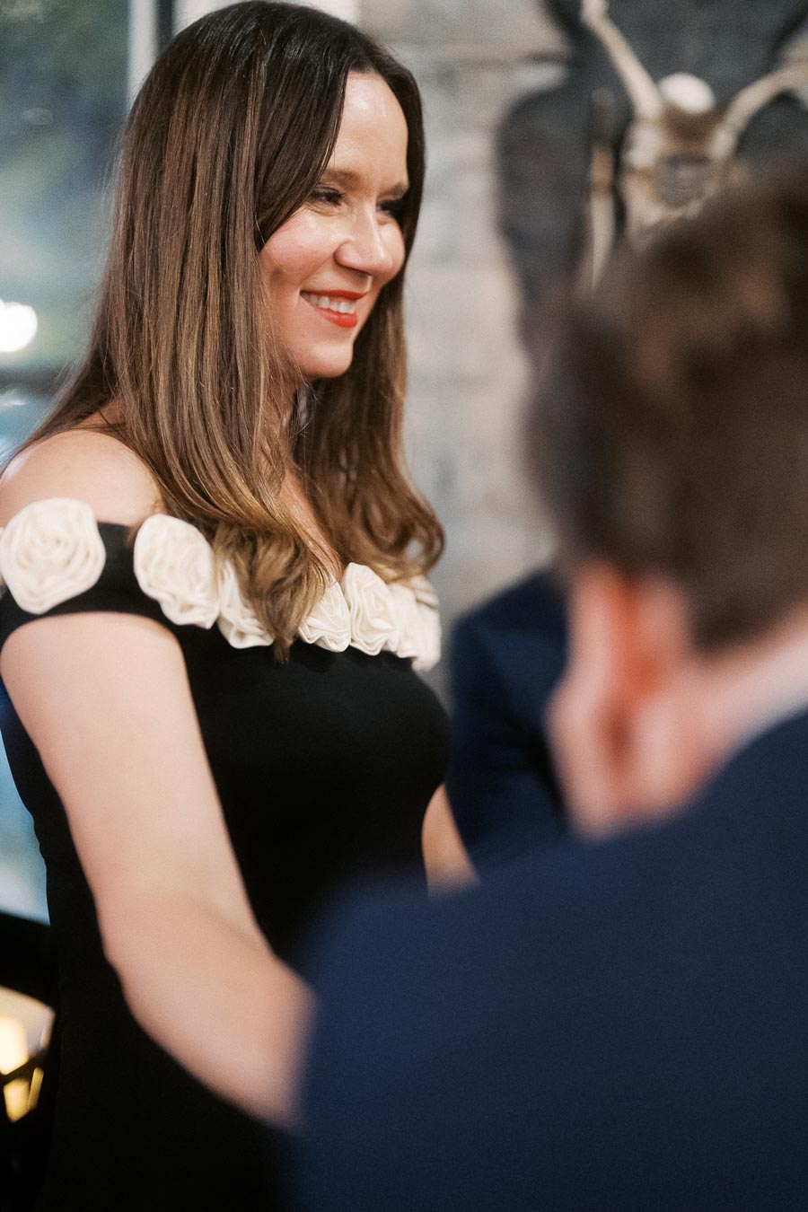 Smiling woman in a stylish black dress with floral accents at a social gathering.