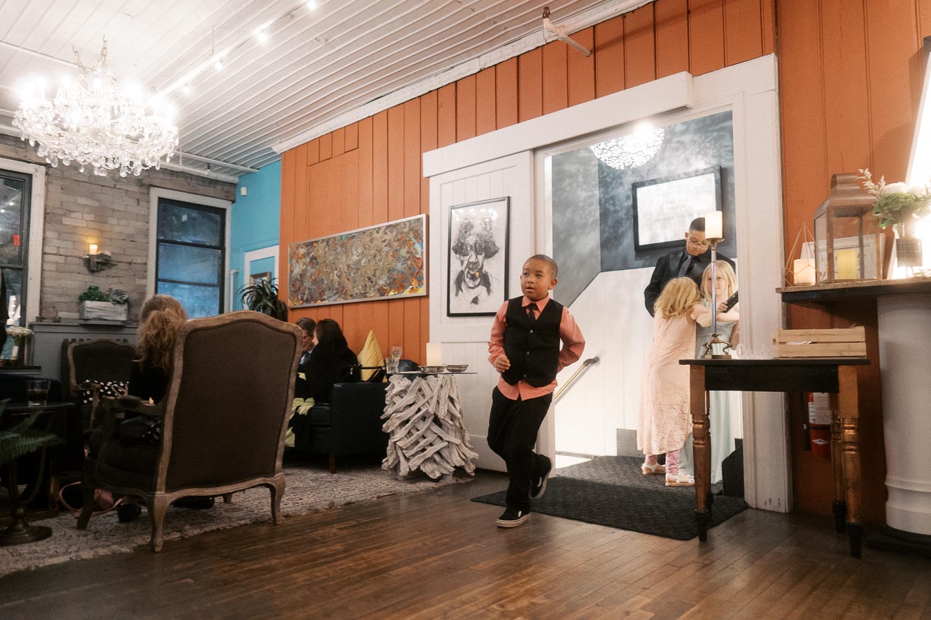 Chic restaurant interior with children in formal attire, featuring warm lighting, decorative artwork, and vintage furniture, creating an inviting ambiance.