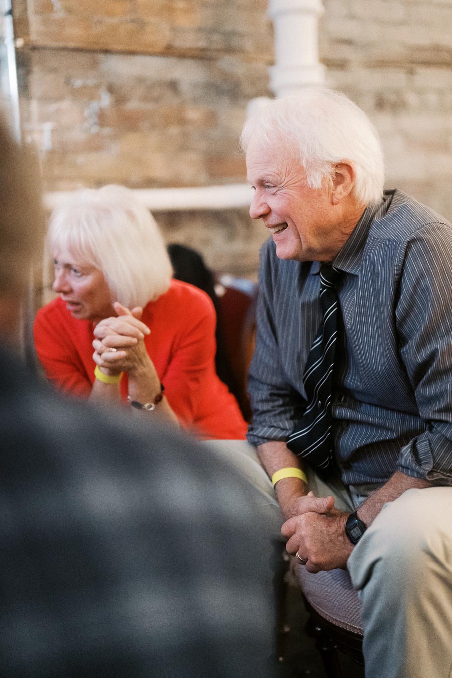 Elderly couple smiling and enjoying a conversation in a cozy setting with a brick wall backdrop.