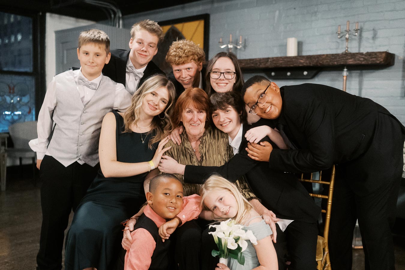 A heartwarming family gathering featuring a group of smiling individuals of various ages, dressed formally, embracing in a cozy indoor setting.