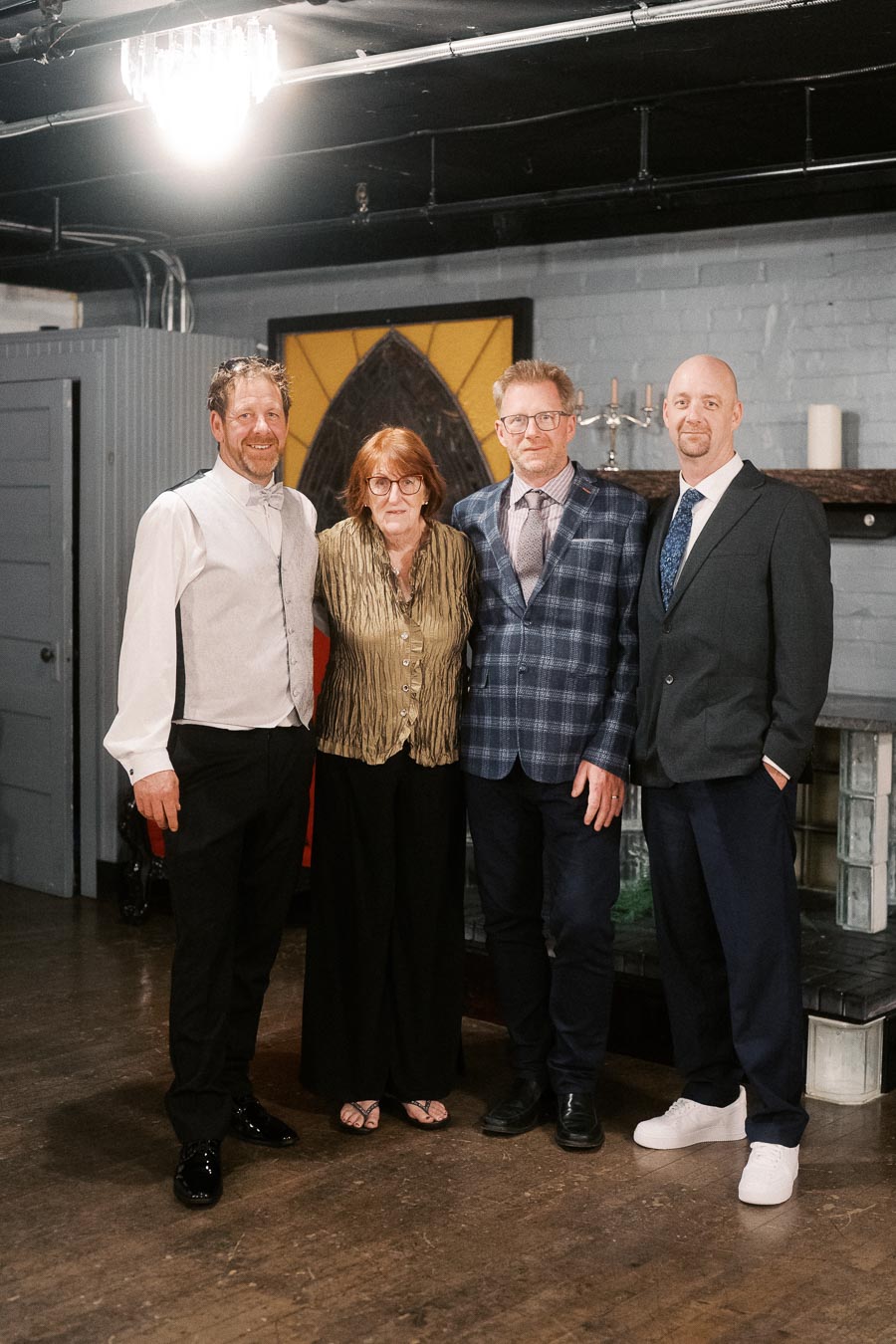 Group of four people dressed in formal attire standing indoors with a wooden floor and modern decor.