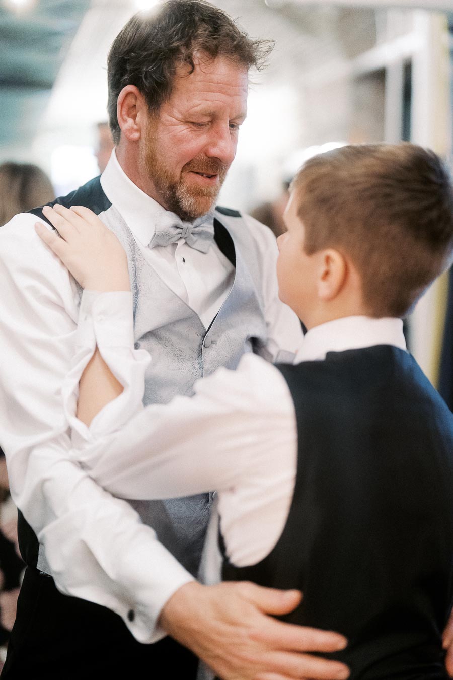 Father and son dressed in formal attire share a dance at a wedding reception, emphasizing family bonds and celebrations.
