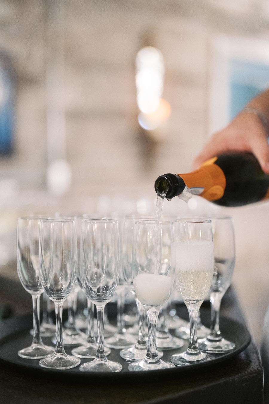 A close-up of a hand pouring champagne into a row of elegant flute glasses on a tray, perfect for a celebration or festive event.