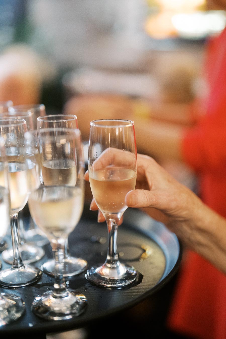 A tray of filled champagne flutes, with a hand elegantly holding one glass, set in a festive gathering ambiance.