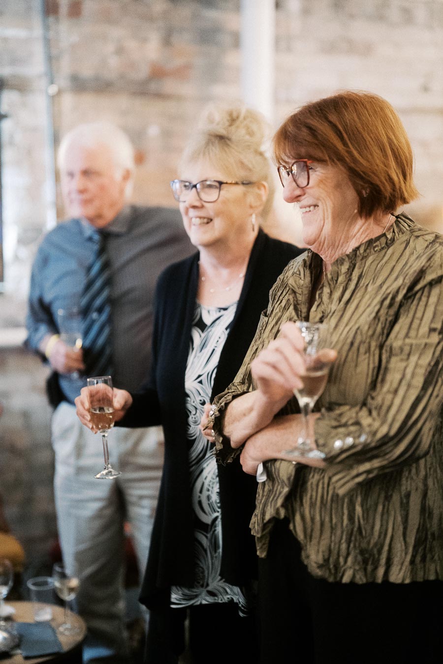 Elderly friends enjoying a social gathering indoors, wearing formal attire and holding drinks, with smiles on their faces.