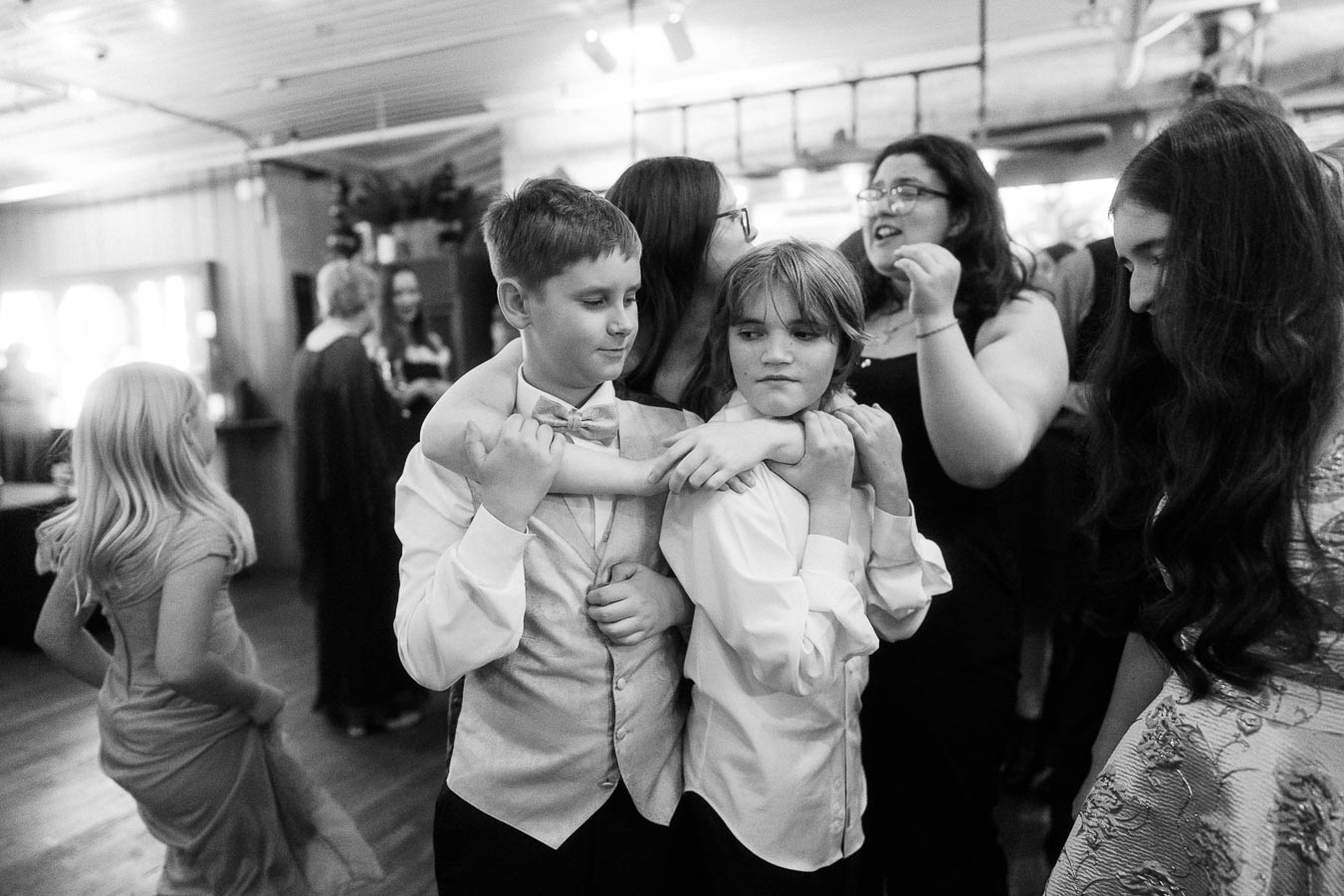Black and white photo of a lively social gathering with children dressed in formal attire, playfully interacting amidst a cheerful group setting.
