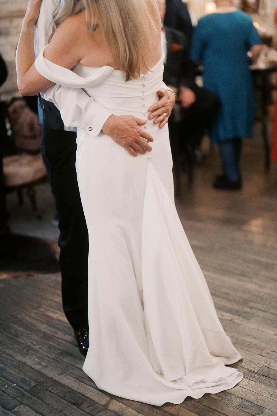 A couple dancing closely at their wedding, with the bride wearing an elegant white gown and the groom in a formal suit, captured on a rustic wooden floor.