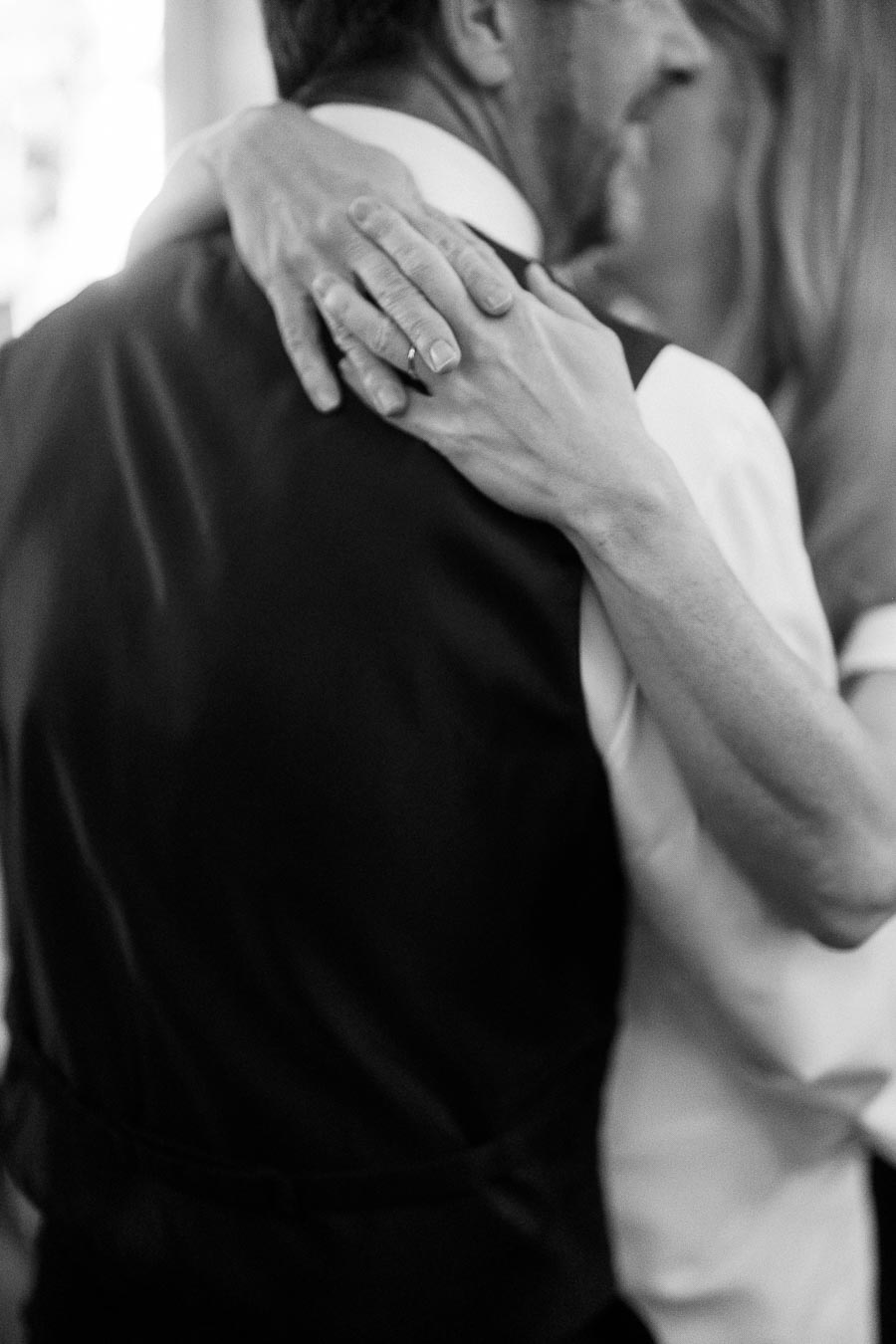 Close-up black and white image of a couple embracing, showcasing the woman's hand gently resting on the man's back, emphasizing intimacy and connection.