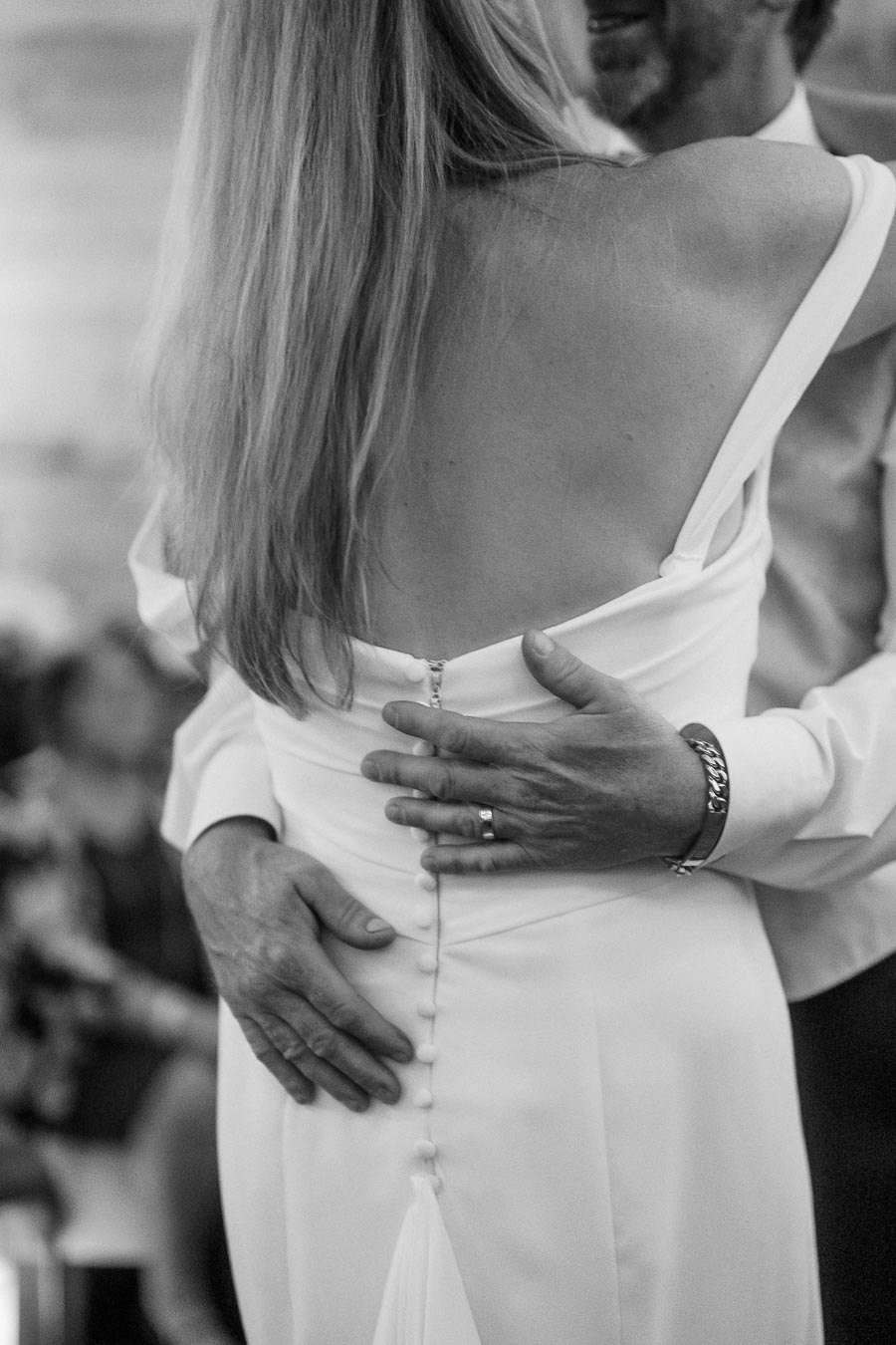 Elegant back view of a bride in a white buttoned wedding dress dancing with a partner, showcasing a romantic and intimate wedding moment.