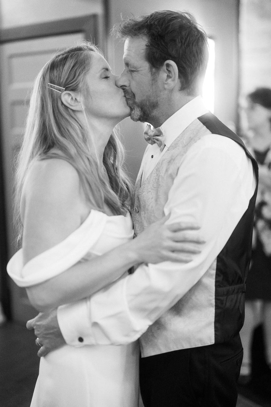 Elegant black and white photo of a couple sharing a tender kiss at their wedding reception, dressed in formal attire.