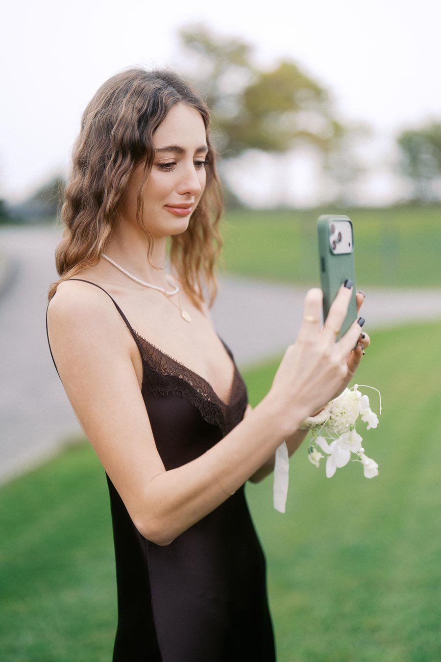Young woman in an elegant black dress using a smartphone outdoors.
