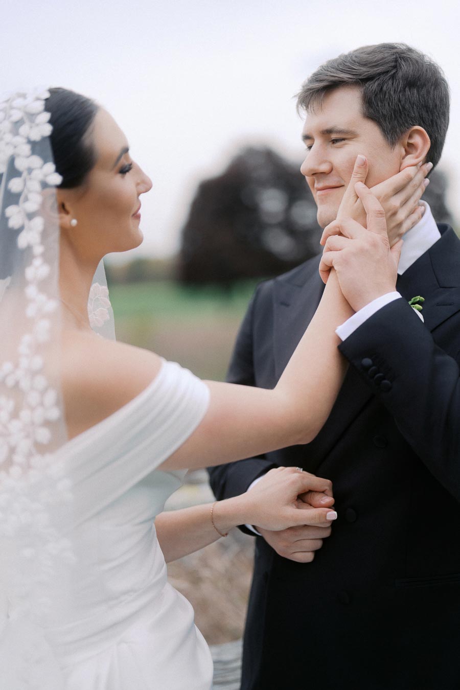 Bride and groom sharing a loving moment on their wedding day, with the bride gently holding the groom's face, in a picturesque outdoor setting.