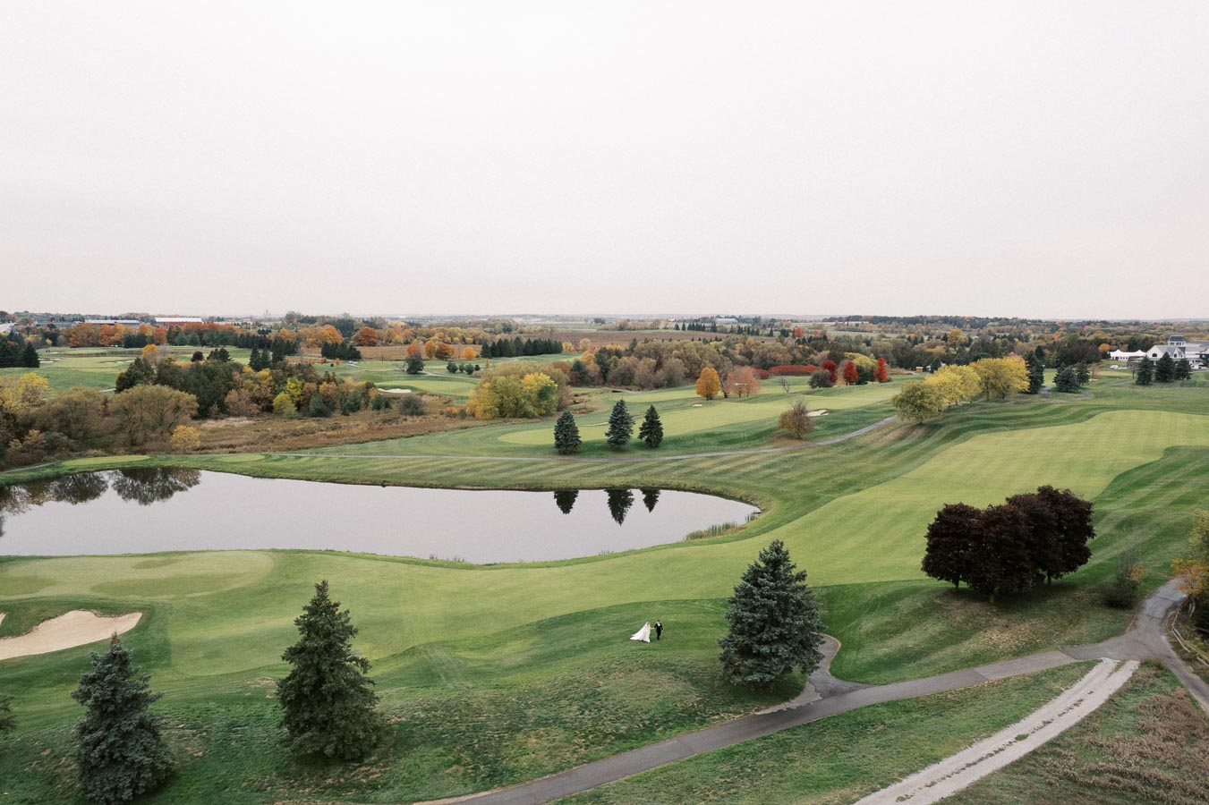 Aerial view of a picturesque golf course in autumn, featuring lush green fairways, a reflecting pond, and colorful trees with fall foliage. Perfect setting for outdoor recreational activities and seasonal photography.