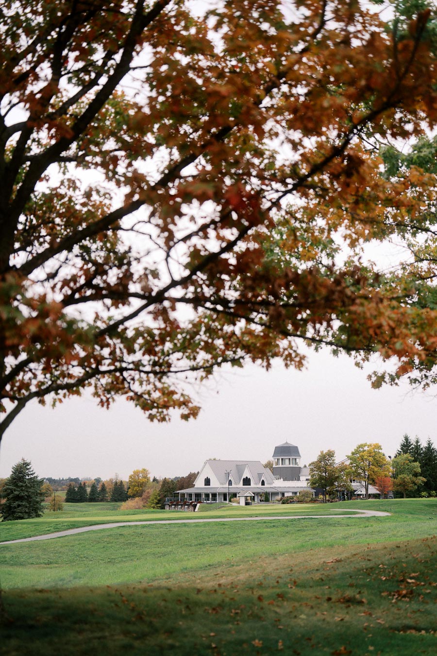 Autumn view of a picturesque white house on a lush green landscape, framed by vibrant fall foliage under a cloudy sky.