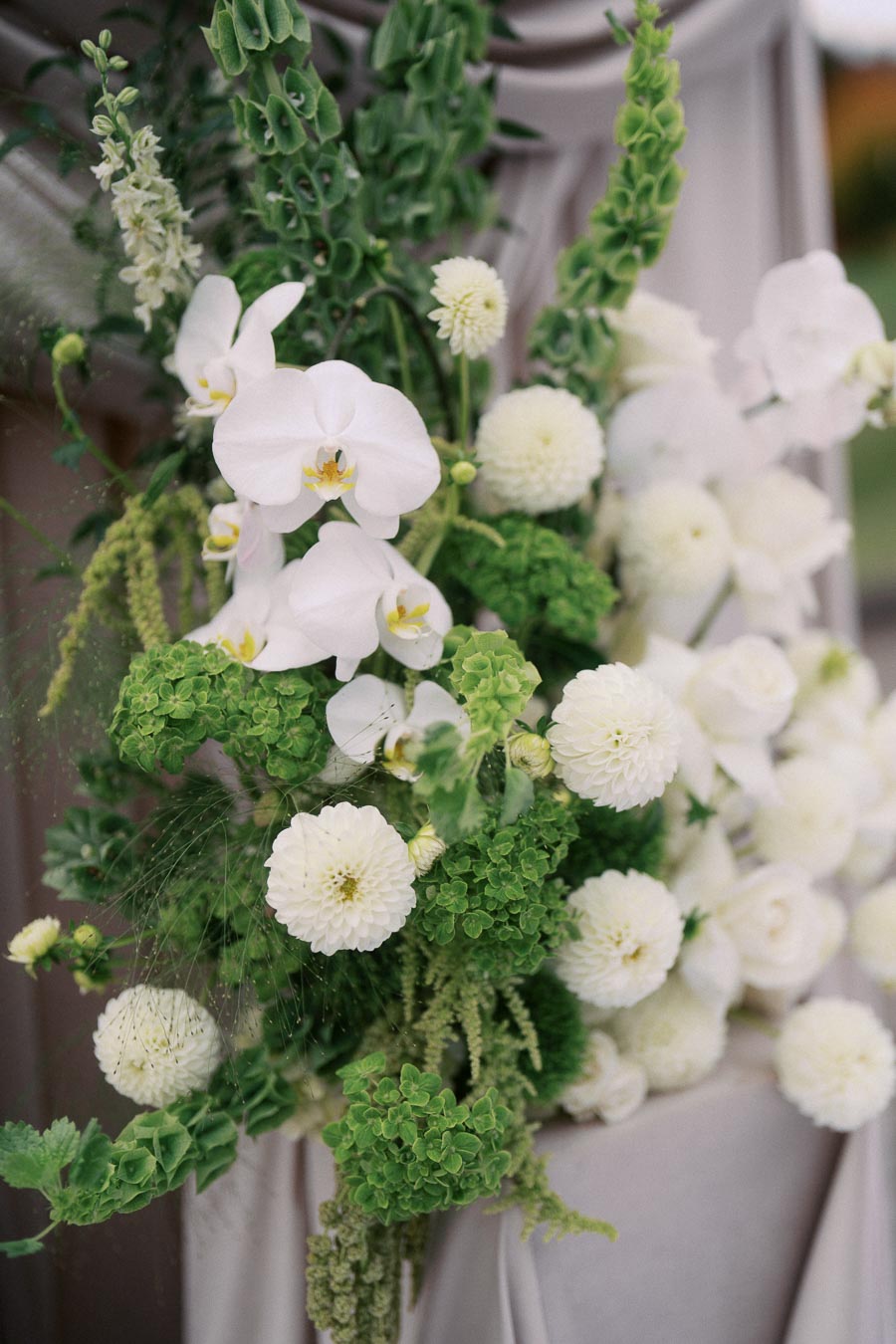 Elegant floral arrangement featuring white orchids, dahlias, and lush green foliage, perfect for weddings and special events.