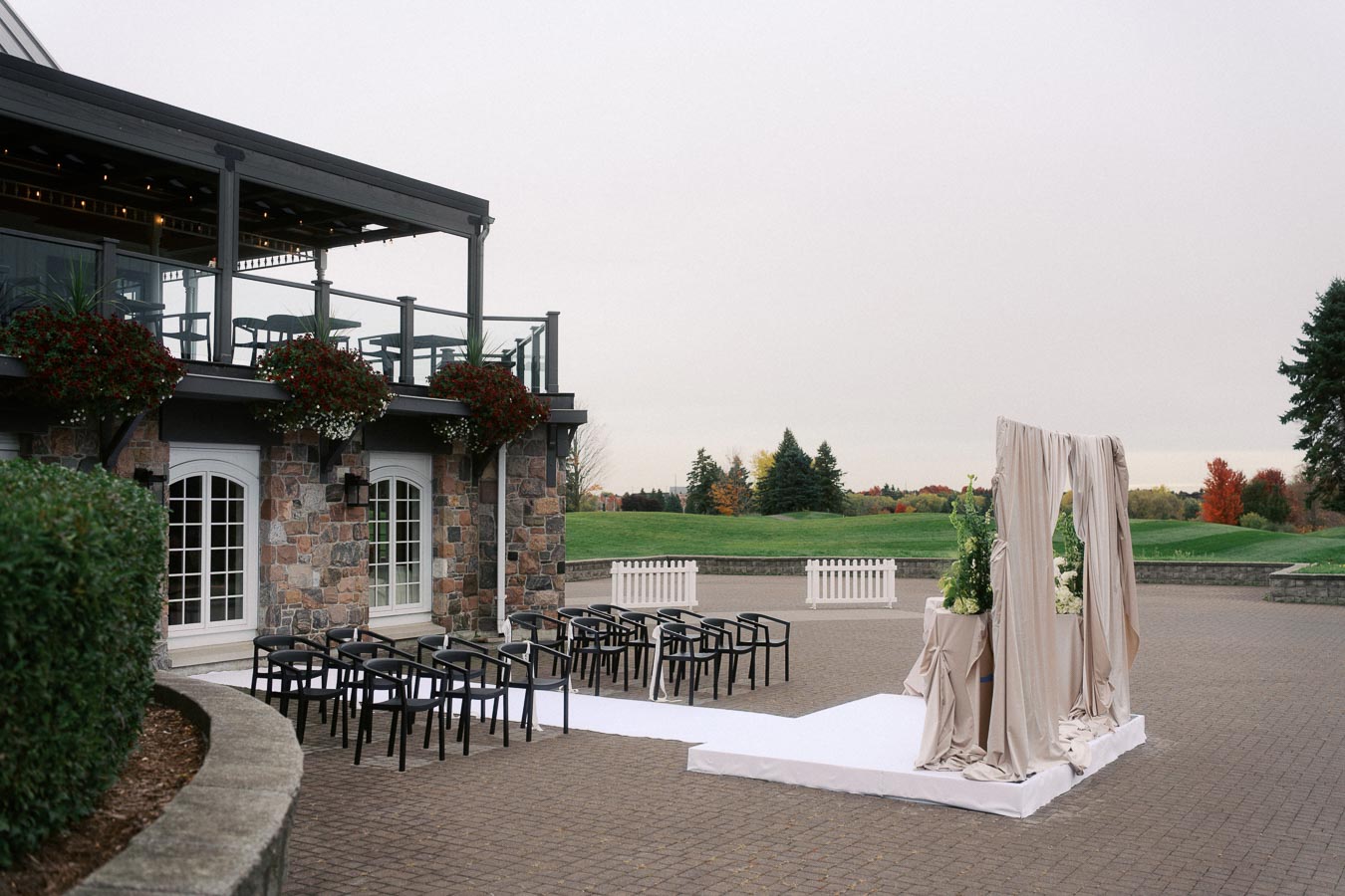 Outdoor wedding ceremony setup with chairs and decorative archway, adjacent to a stone building with a balcony, overlooking a green landscape.