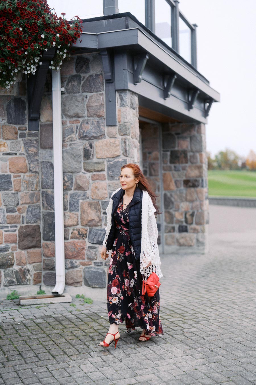 Woman in a floral dress walking by a stone building.