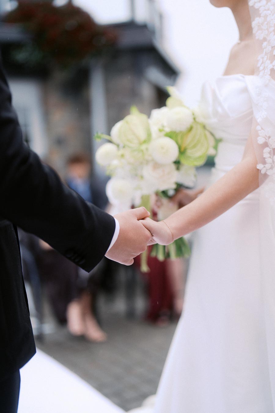A bride and groom holding hands during a wedding ceremony, with the bride wearing a white gown and holding a bouquet of white flowers.