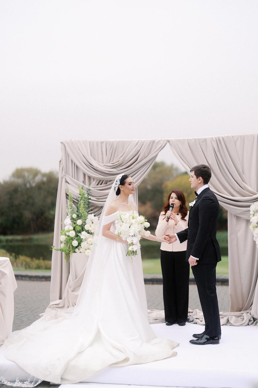 Bride and groom holding hands during an outdoor wedding ceremony with an elegant floral backdrop.
