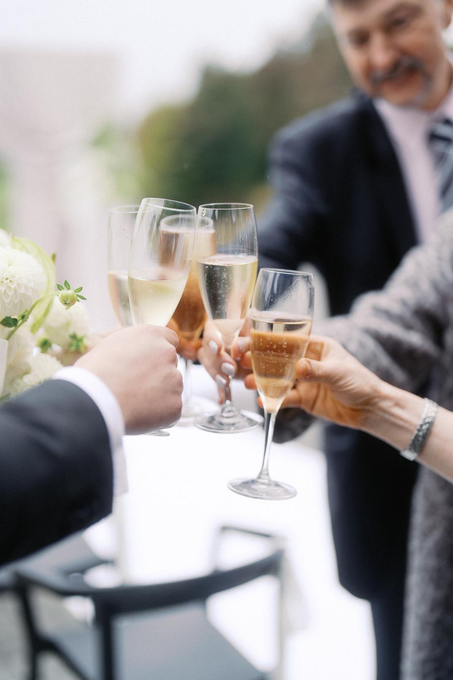 A group of elegantly dressed people toasting with champagne glasses at an outdoor celebration, focusing on the sparkling bubbles and festive atmosphere.
