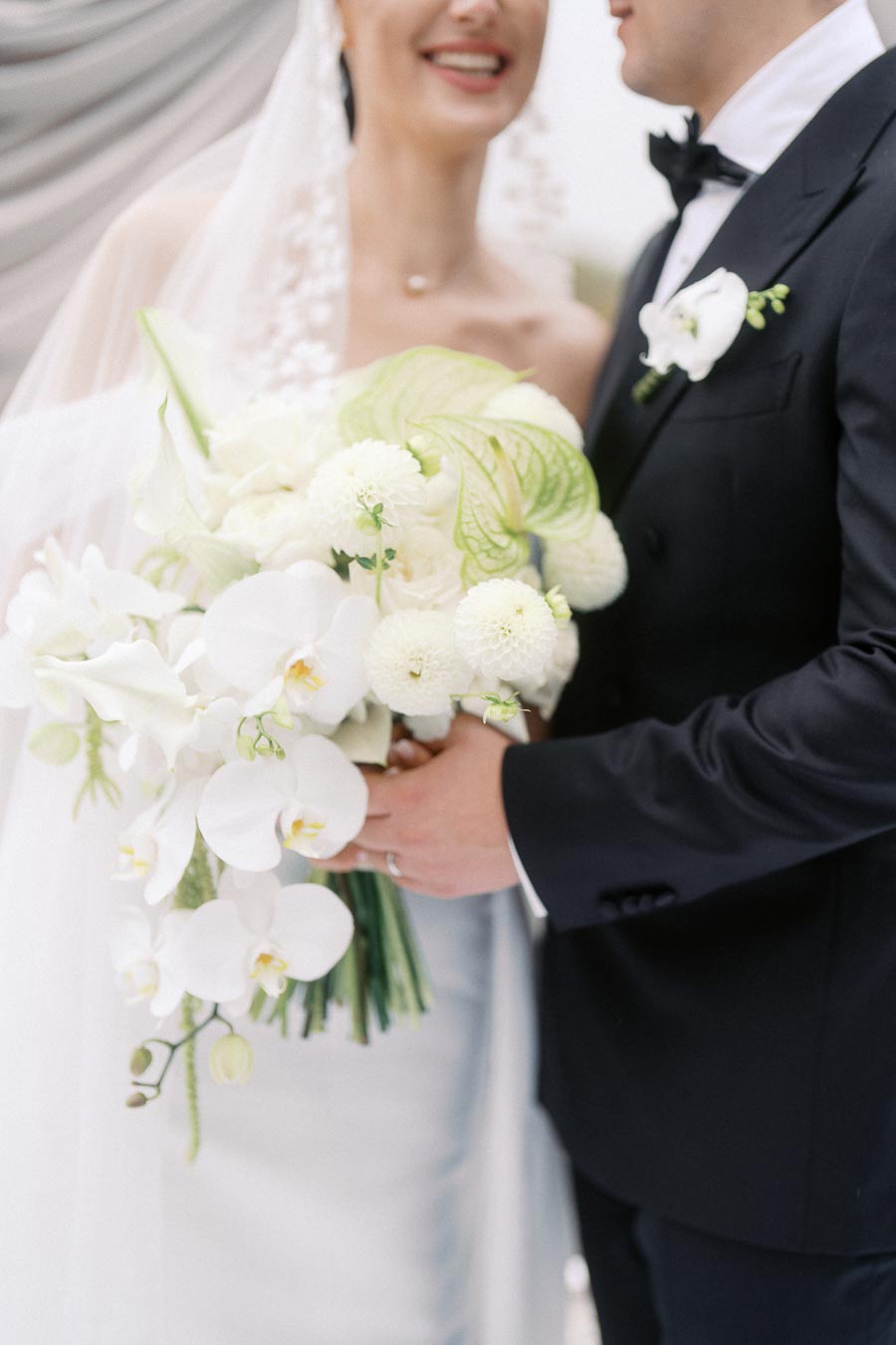 Bride and groom holding a bouquet of white flowers and dressed in formal wedding attire.