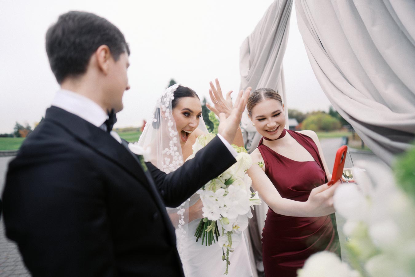 Bride and groom with a bridesmaid taking a joyful selfie at an outdoor wedding, capturing a candid moment of celebration and happiness.